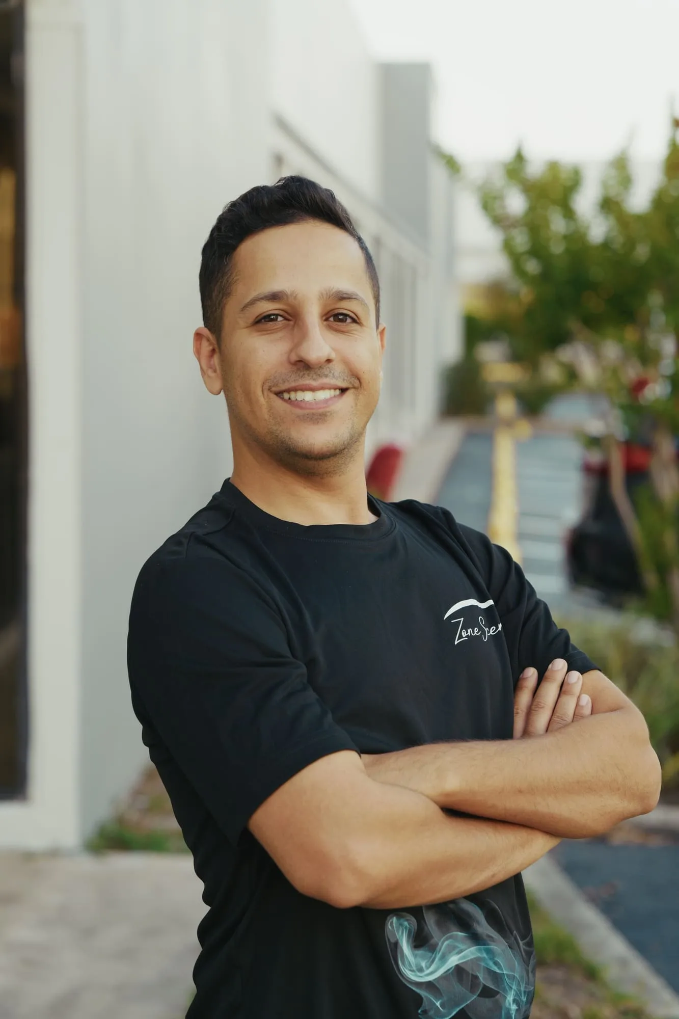 Outdoor portrait of a smiling man in a black T-shirt with his arms crossed