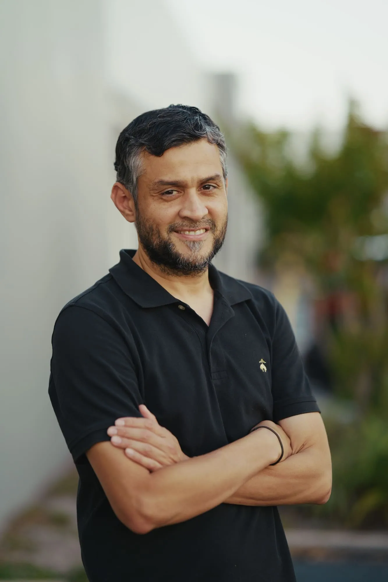 Outdoor portrait of a man in a black polo shirt with his arms crossed
