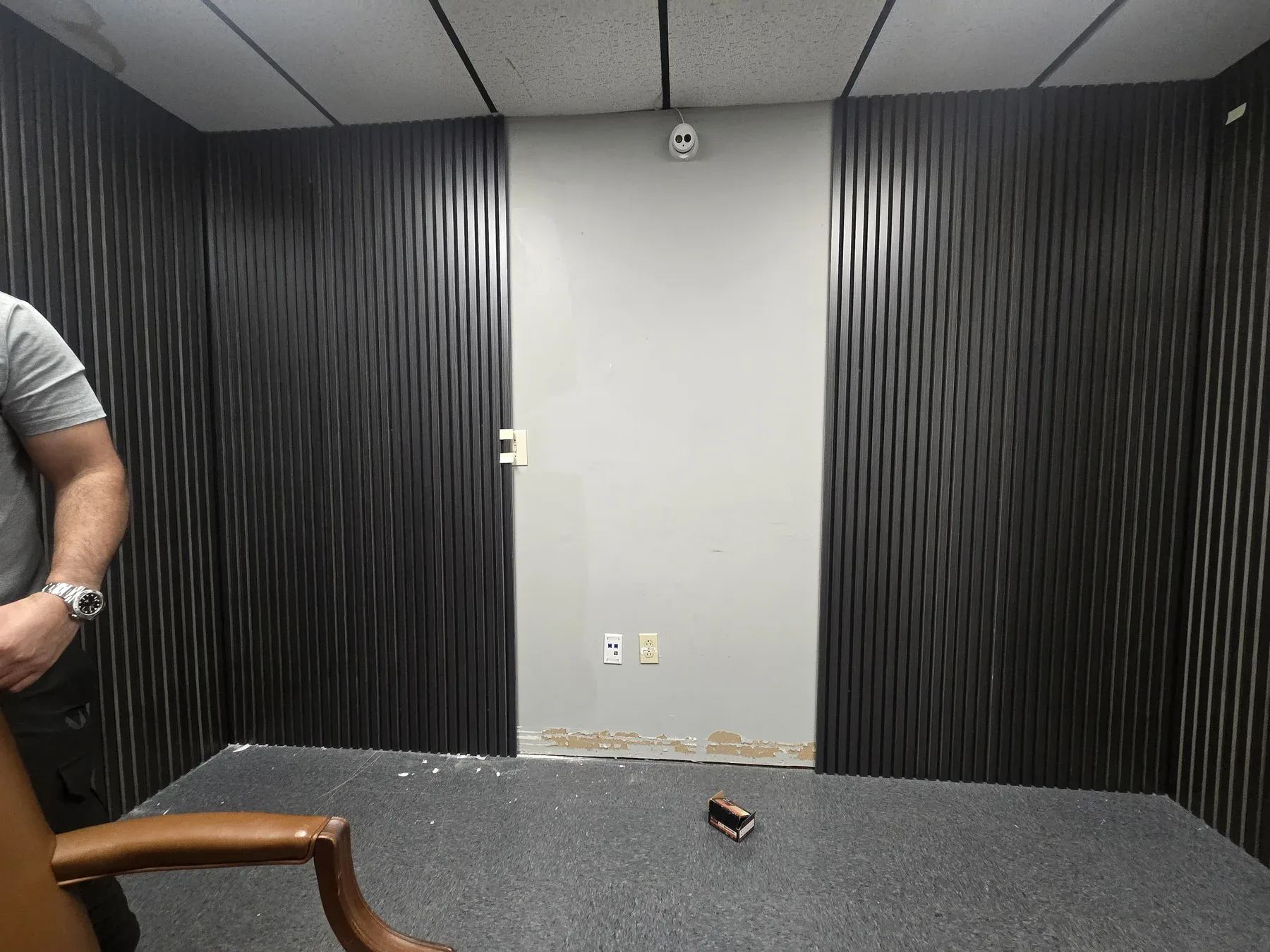 Slatted wall panels fitted around an unfinished center section of the small podcast room