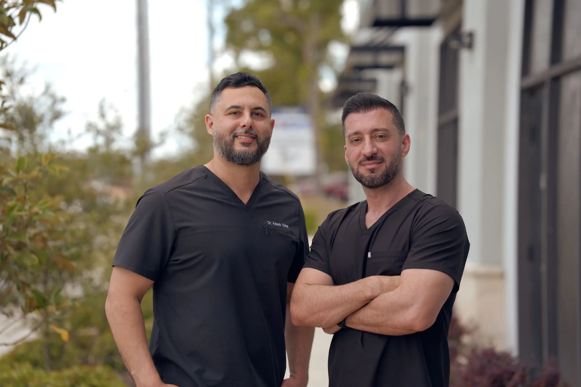Two medical professionals posing together outdoors in black scrubs
