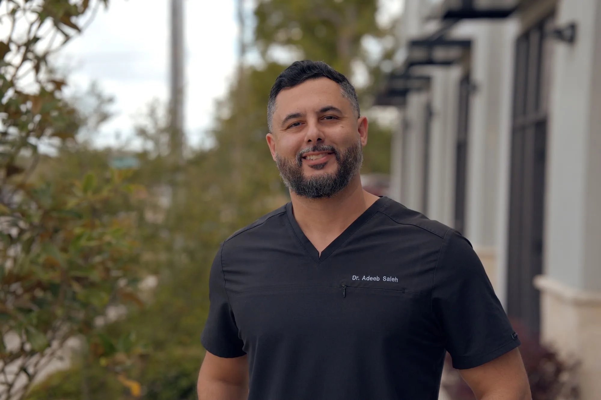 Outdoor professional portrait of a smiling doctor wearing black medical scrubs