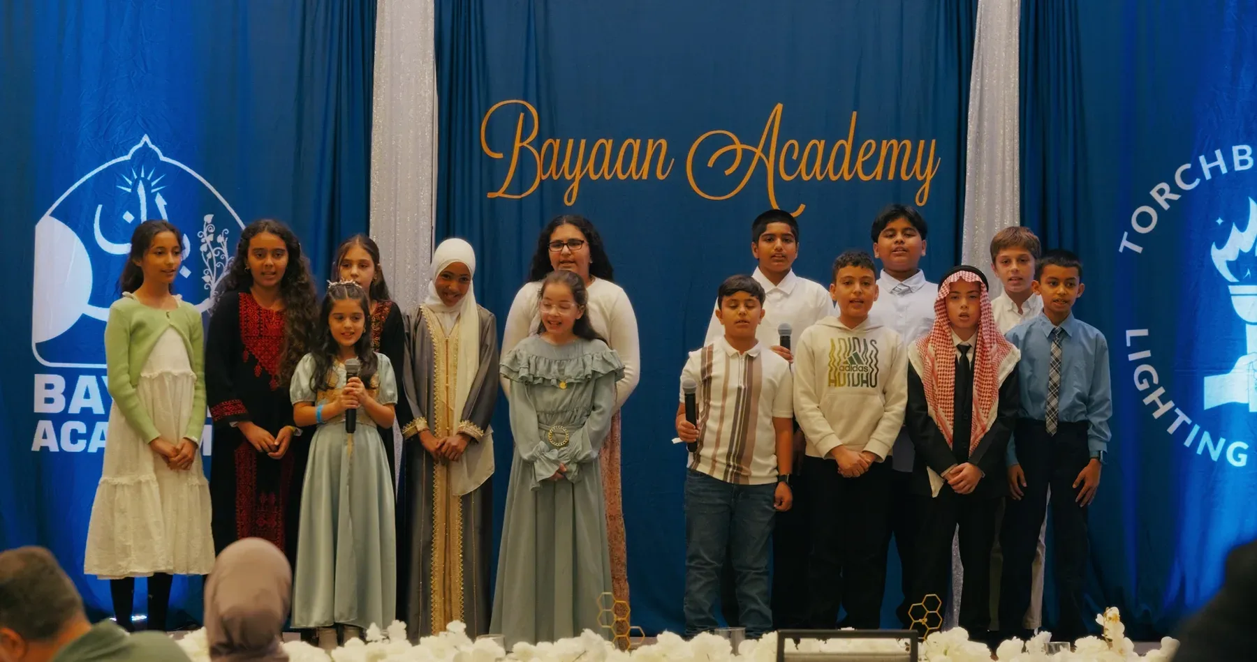 Bayaan Academy students standing together onstage during a fundraising event