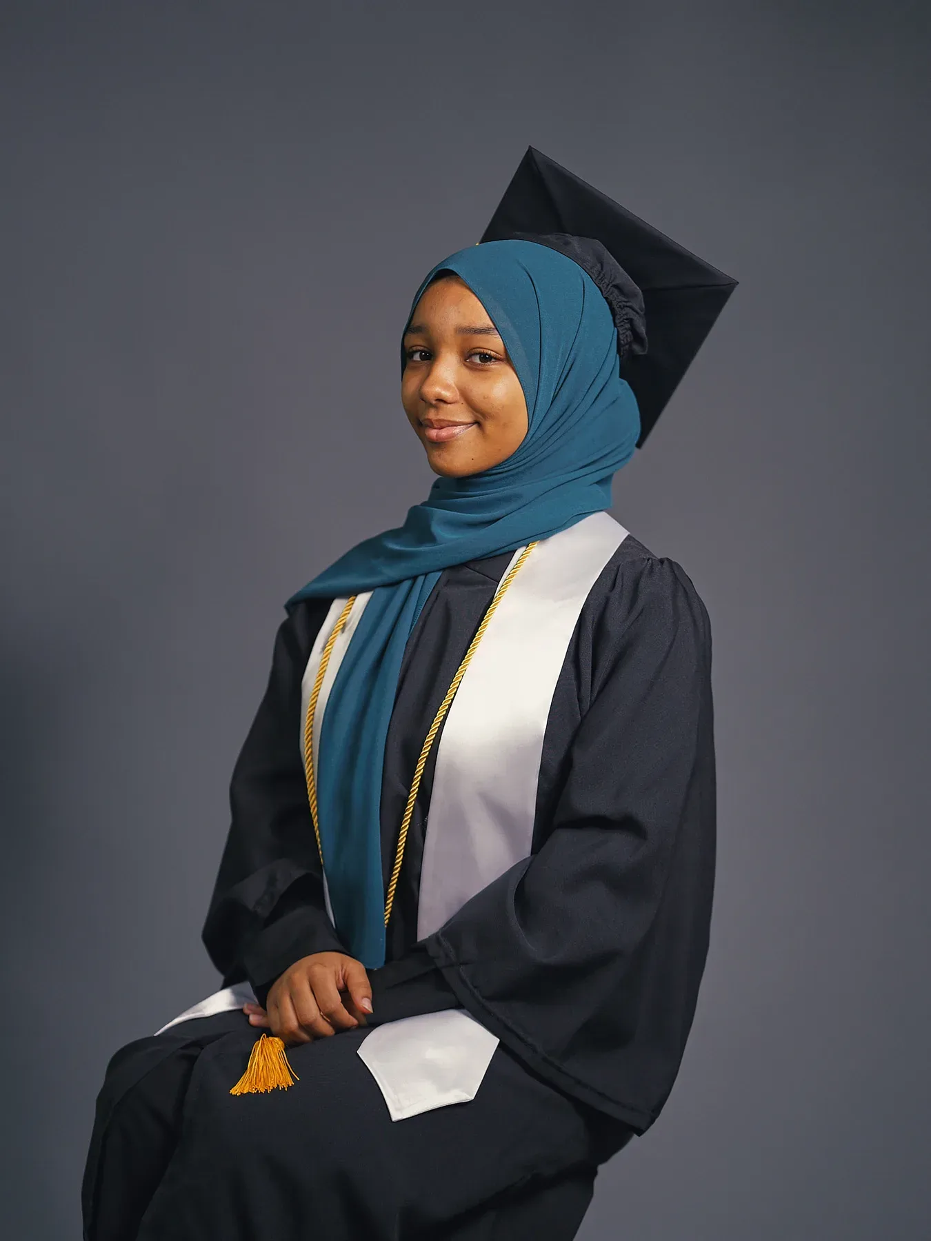 Bayaan Academy graduate wearing a navy cap and gown with a blue hijab