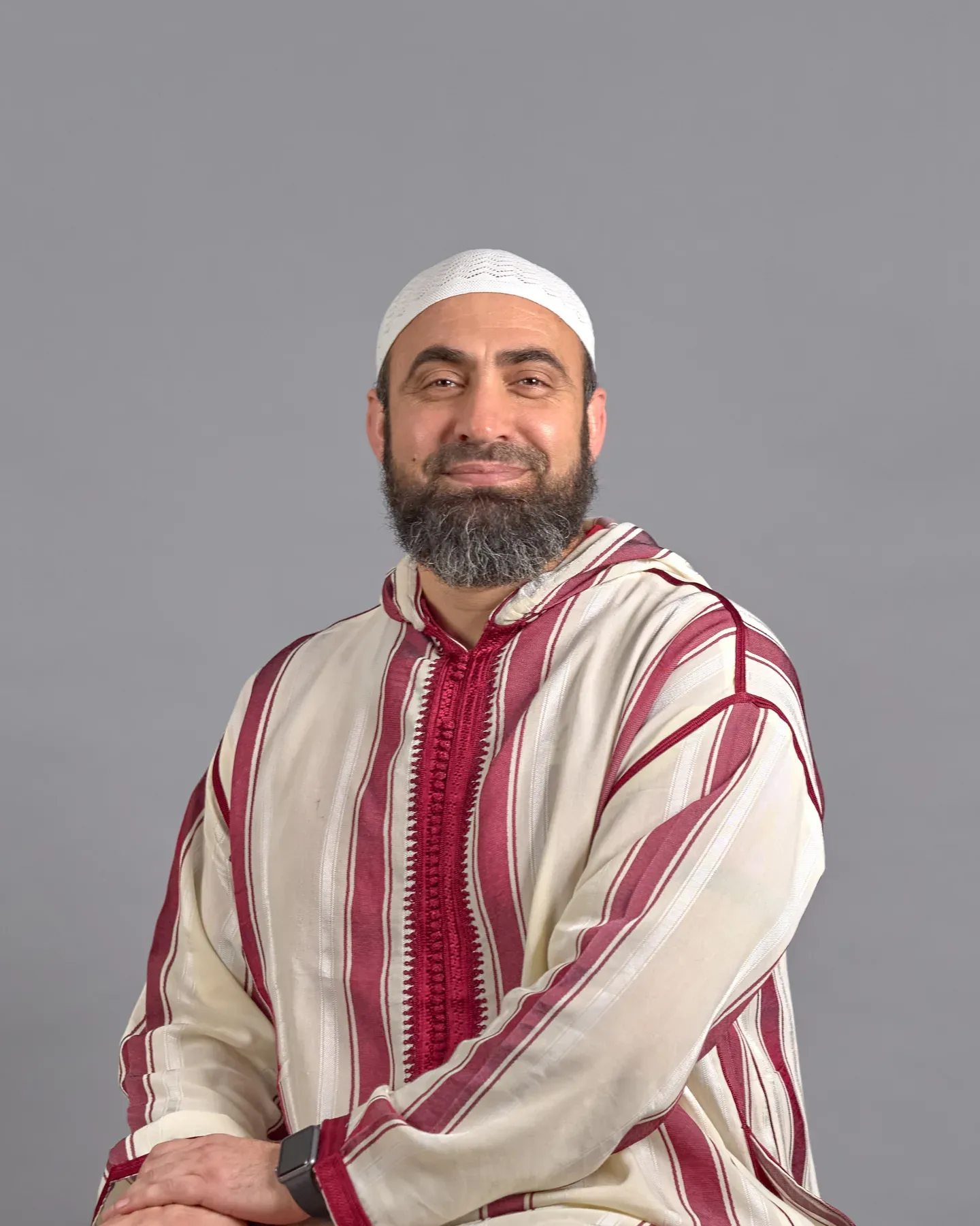 Bayaan Academy staff member in a red and white thobe against a gray portrait background